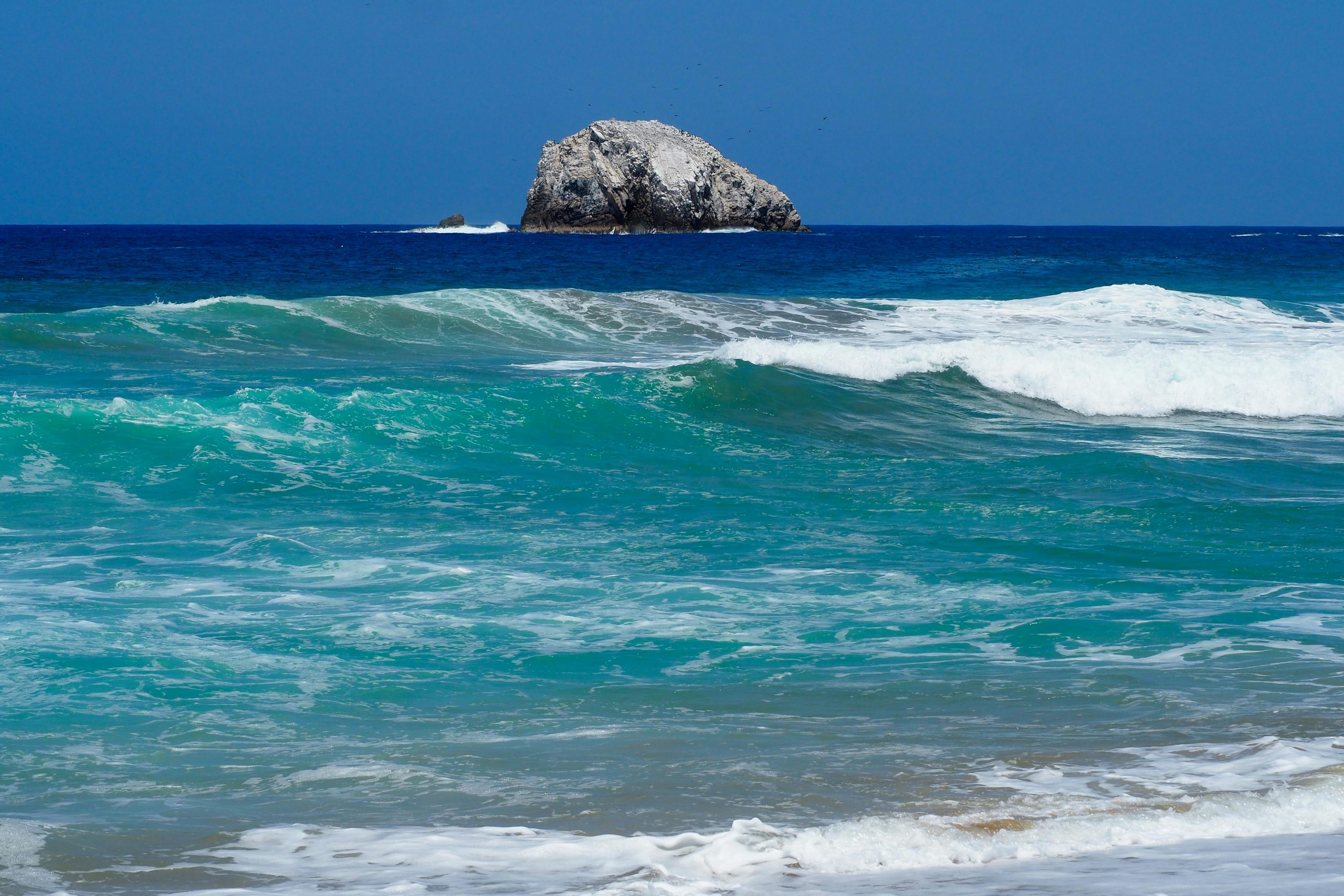 Vibrant ocean waves and rock formation off the coast of Oaxaca, Mexico.