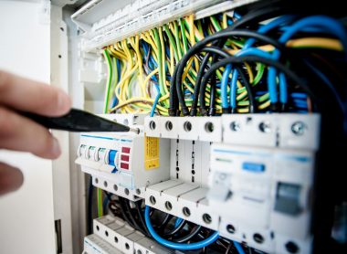 Hand of electrician working on a circuit breaker panel with colorful wires, ensuring safe electrical connections.